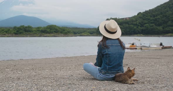 Woman sit at the lake side with a wild cat in shojiko of Japan