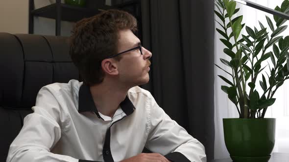 Young businessman is sitting at modern office desk, closing laptop computer and finishing to work