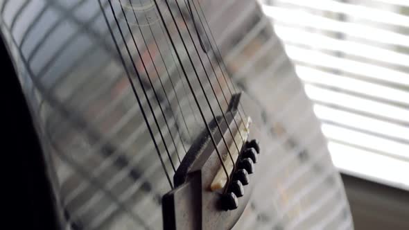 Black shiny acoustic guitar on a stand by the window, CLOSE UP