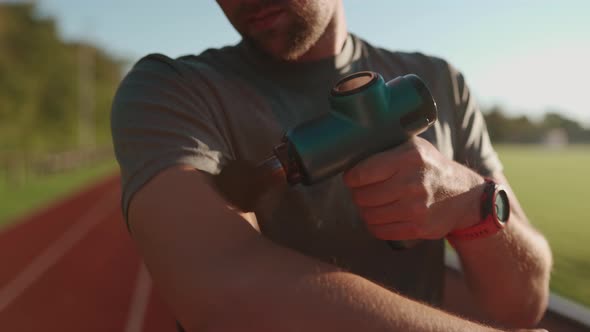 An Athlete Massages with a Percussion Therapy Gun to Relieve the Pain of Muscle Aches After a