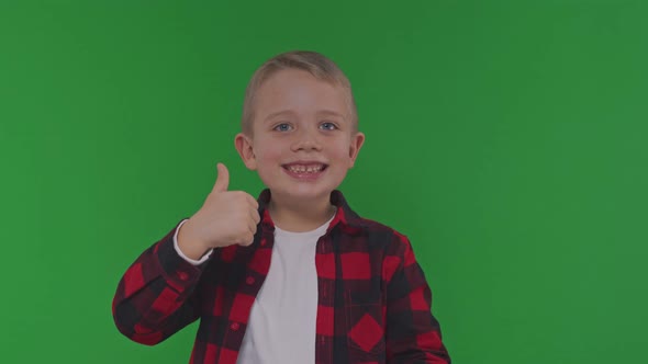 Funny Little Boy Smiles and Shows Thumbsup Posing for Camera on Green Background Close View