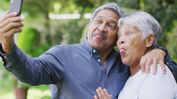 Video of happy biracial senior couple embracing and taking selfie in garden