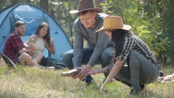 Young Man in Hat Bringing Firewood and Talking with Charming Woman As Blurred Couple of Friends