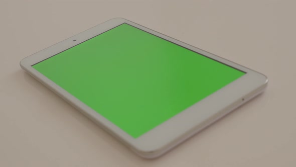 Tablet PC with green screen on display tilting on white surface 4K 2160p UltraHD footage - Slow tilt