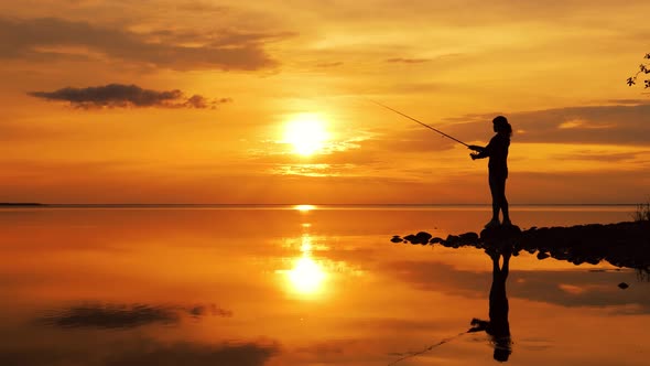 Woman Fishing on Fishing Rod Spinning at Sunset Background