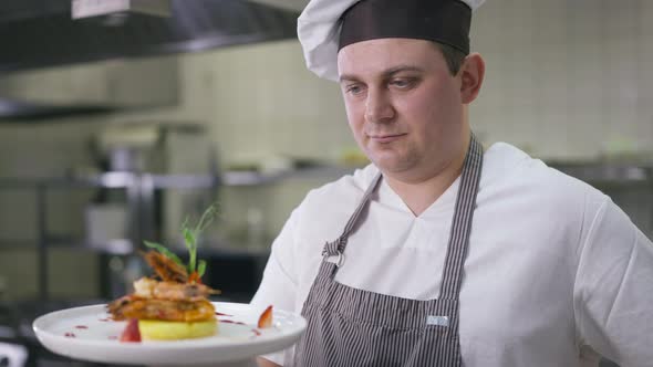 Portrait of Professional Cook in Hat and Apron Posing with Cooked Tasty Seafood Indoors in Kitchen