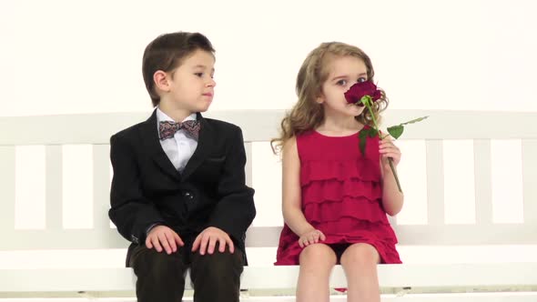 Little Boy Gives a Rose To His Girlfriend and Kisses Her on the Cheek. White Background. Slow Motion