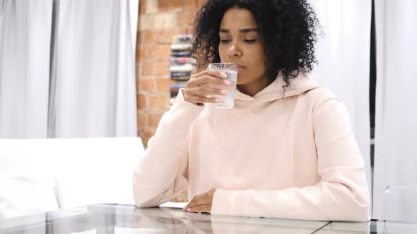 AfroAmerican Woman Drinking Water From Glass and Working on Laptop