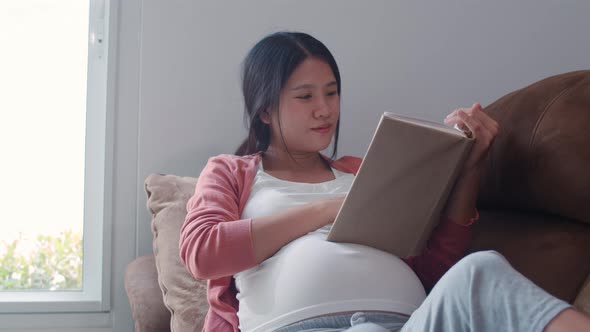 Young Asian Pregnant woman using tablet search pregnancy information feeling happy smiling.