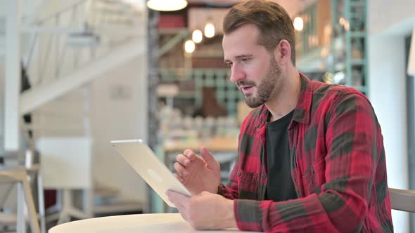 Young Man Celebrating Success on Tablet in Cafe 