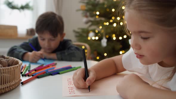 Writing letter to Santa Claus by cute little girl with her brother