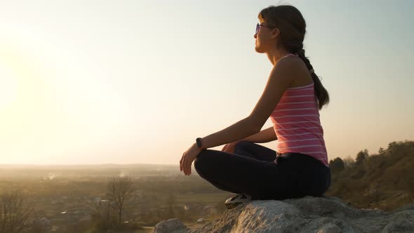 Young relaxed woman sitting outdoors on a big stone enjoying warm summer day. Girl meditating