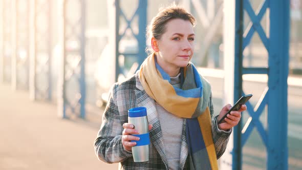 Caucasian Businesswoman in a Coat Walking Across the Bridge on a Frosty Morning Drinking Coffee and