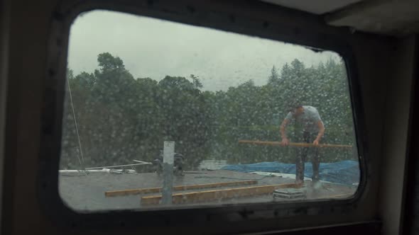 View through rainy boat window young man puts on jacket