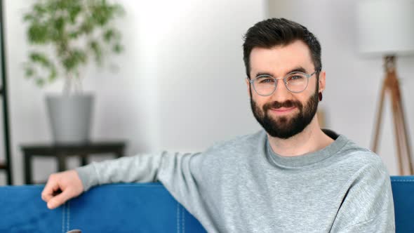 Handsome Bearded Man Friendly Smiling Resting on Comfortable Blue Couch Apartment Interior Portrait