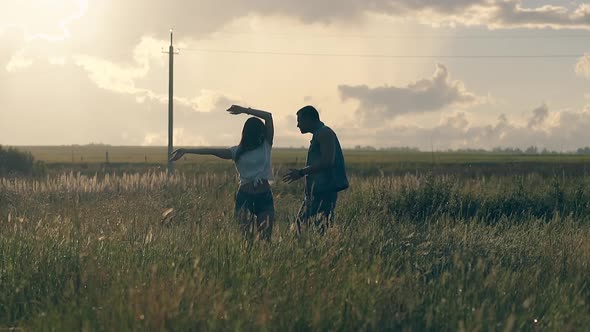 Long Haired Girl Dances with Man on Meadow in Evening