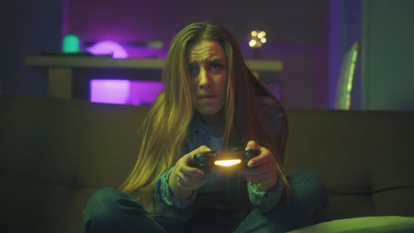 A Beautiful Excited Young Gamer Girl Is Sitting on a Couch and Playing Video Games on a Console