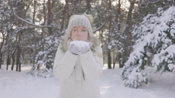 Happy Cute Girl Dressed in Warm Winter Clothes Blows Snow From Her Hands to the Camera Then Tosses