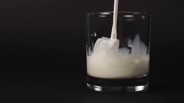 Pouring fresh milk into a glass with ice cubes on a black background.