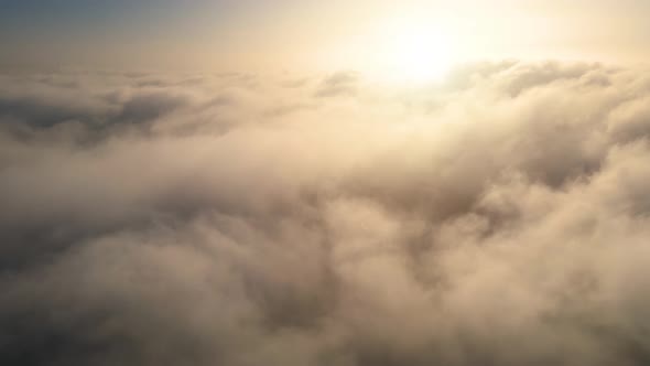 Aerial shot of flying over a layer of soft clouds at dawn