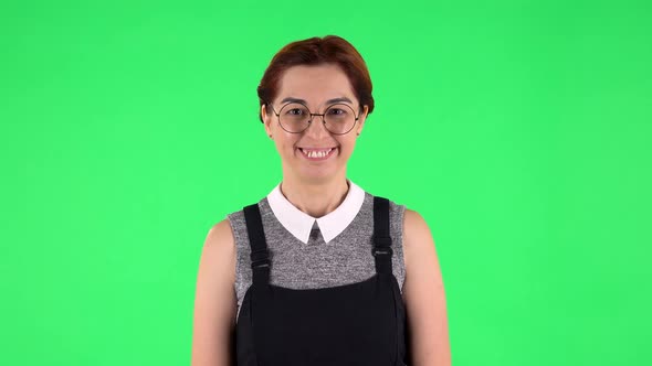 Portrait of Funny Girl in Round Glasses Is Smiling While Looking at Camera. Green Screen