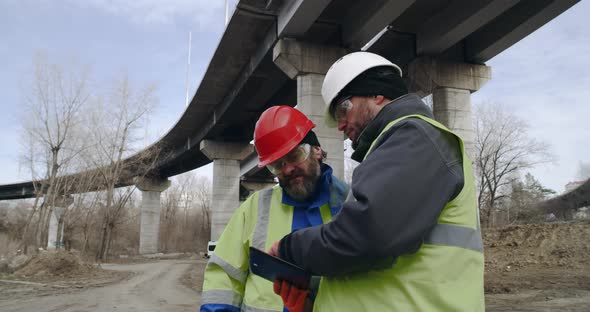 Male Builders with Tablet Discussing Data in Outskirts