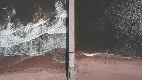 Aerial birds eye view drone footage of a waves crashing onto the beach against a pier, Roker Beach,