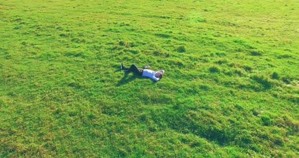 Low Orbital Flight Around Man on Green Grass with Notebook Pad at Yellow Rural Field.