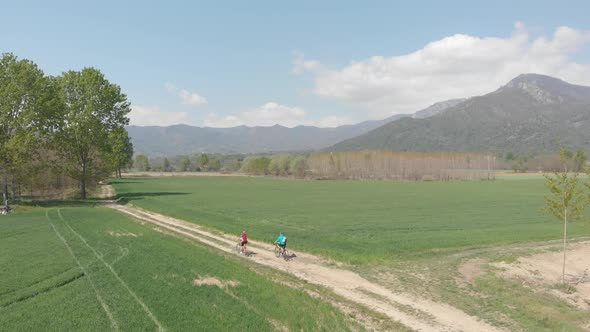 Couple having fun by riding mountain bike on dirt road in sunny day, scenic landscape of snowcapped