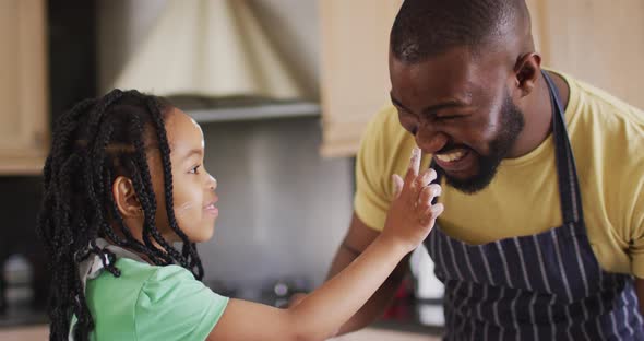 Happy african american father and daughter baking, playing with flour in kitchen