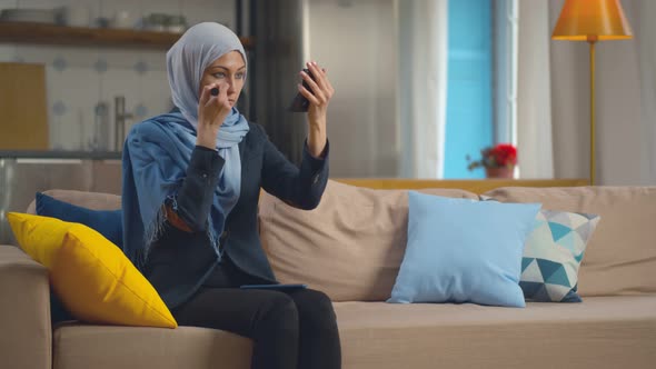 Beautiful Woman in Hijab Applying Make-up Sitting on Couch in Living Room