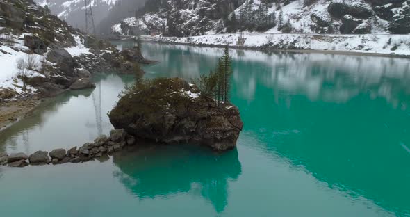 flying over a big stone island with spruces over blue cyan water during heavy snow