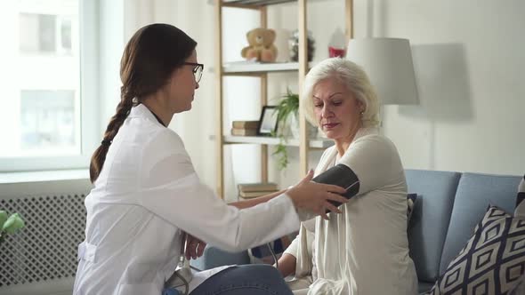 Young Nurse Measuring Blood Pressure and Visit Senior Woman