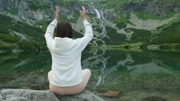 Young Woman Meditating and Holding Up Hands Under the Head with Amazing View on the Lake