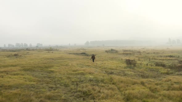 Young documentarist wading through tall grass,misty moorland,Czechia.