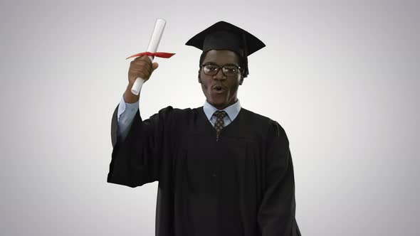 Happy African American Male Student in Graduation Robe Walking Towards Camera Waving His Diploma on