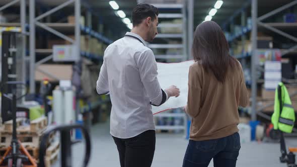 Back View Focused Designers Analyzing Blueprint Standing in Industrial Warehouse