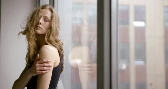 Portrait of a Slender Model Posing on the Windowsill of a Large Panoramic Window. Her Hair Is