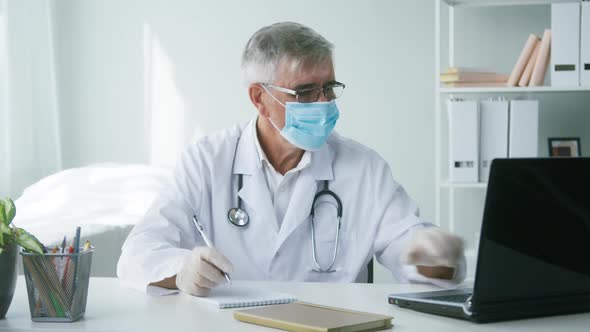 Elderly Grayhaired Doctor in Face Mask and Gloves Writing Notes Using Laptop Portrait of Male