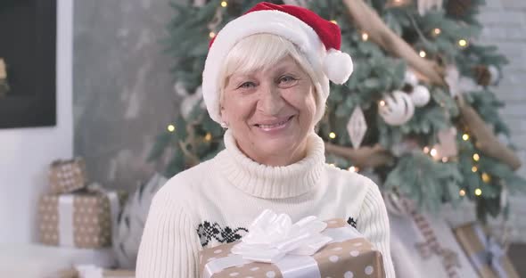 Close-up Portrait of Positive Senior Caucasian Woman Holding Christmas Gift Box, Looking at Camera
