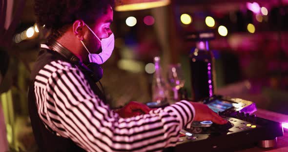 Dj mixing outdoor at cocktail bar - African young man mixing music while wearing safety mask
