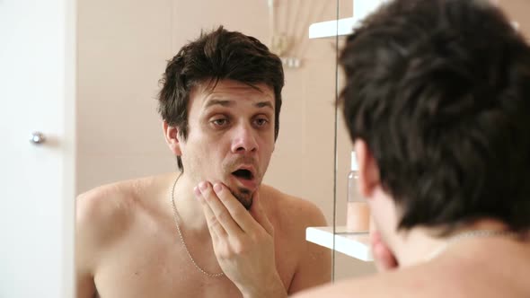 Tired Man Who Has Just Woken Up Looks at Its Reflection in the Mirror, Surprised and Frightened.