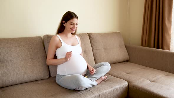 Pregnant Woman Applying Headphones in the Sofa