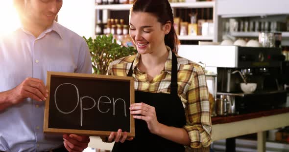 Man and waitress holding chalkboard with open sign
