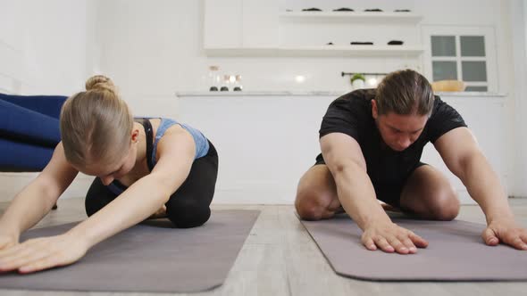 Young American couple in sportswear doing yoga exercise working out in kitchen at home morning.