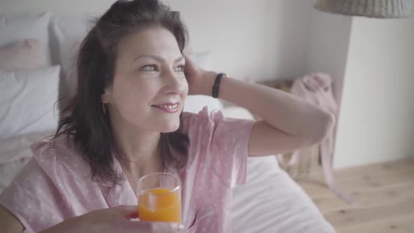 Face of Beautiful Brunette Caucasian Woman Adjusting Hair and Smiling. Happy Lady with Orange Juice