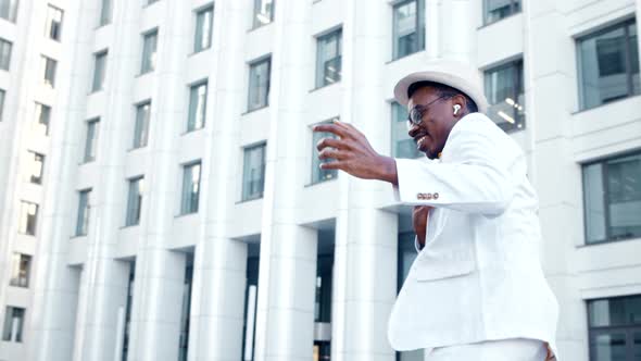 Amazed black man in white suit with hat and glasses listens to music
