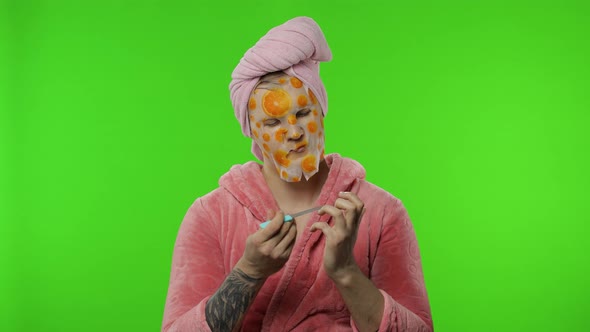 Young Man in Bathrobe with Face Mask Making Manicure. Chroma Key