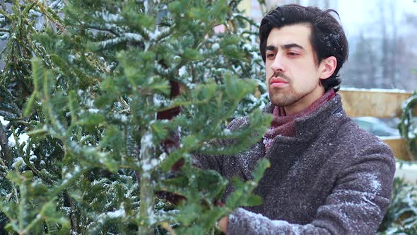 Indian Man in Stylish Wool Coat Buys a Christmas Tree Outdoors Snow Background