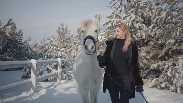 Blonde Strokes and Feeds a White Horse on a Snowy Country Ranch